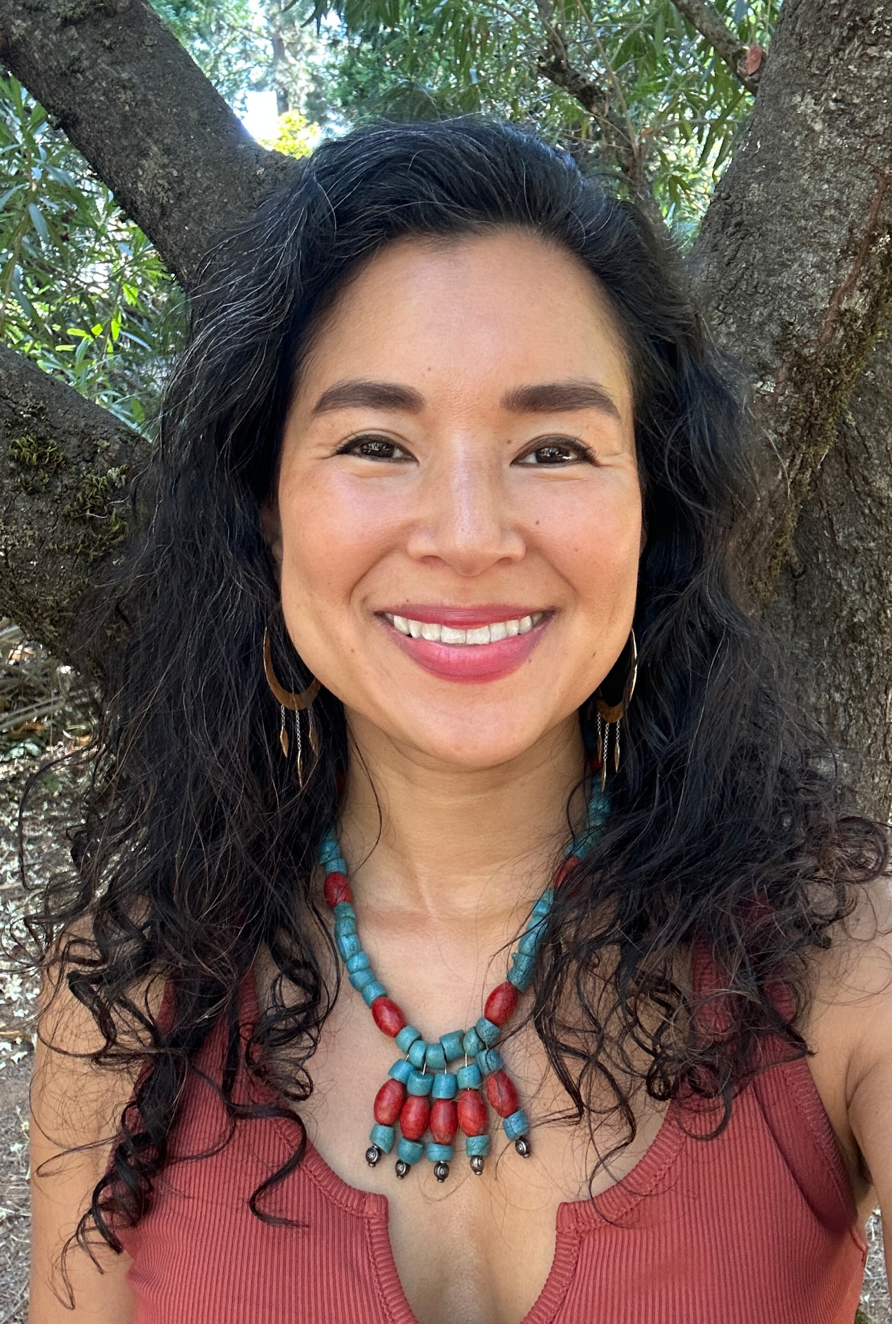 Aimi smiling outdoors wearing a turquoise and red necklace